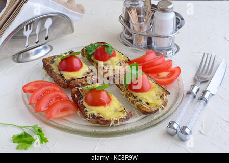 Toasts with aubergine, cheese and tomato on a glass plate on a white abstract background. Quick breakfast or snack. Stock Photo