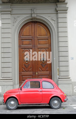 Red Fiat 500 parked on the street in front of an old brown wood entrance. Classic vintage model. Florence, Italy Stock Photo