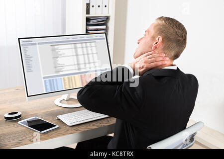 Young Businessman Suffering From Neck Ache While Using Computer At Office Stock Photo