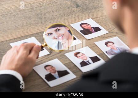 Close-up Of A Businessman Viewing Candidates Through Magnifying Glass At Desk In Office Stock Photo