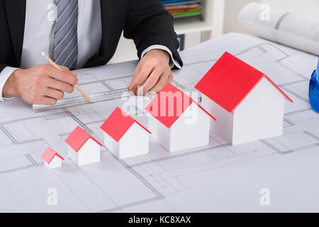 Close-up Of Male Architect Hand With House Models Working On Blueprint In Office Stock Photo