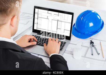 Male Architect Analyzing Blue Print On Computer Over Blue Print In Office Stock Photo