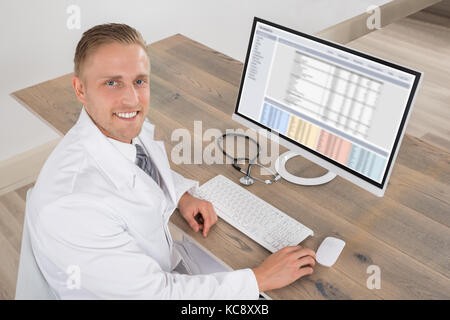Happy Young Doctor Working On Computer At Desk Stock Photo