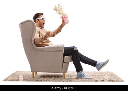 Terrified guy with 3D glasses and popcorn sitting in an armchair isolated on white background Stock Photo