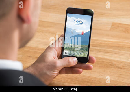Close-up Of Businessman Hand Holding Mobile Phone With Low Battery At Desk Stock Photo