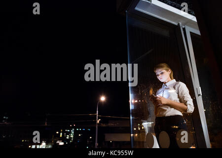 Beautiful young businesswoman with tablet in the office working late at night. Shot through glass. Stock Photo