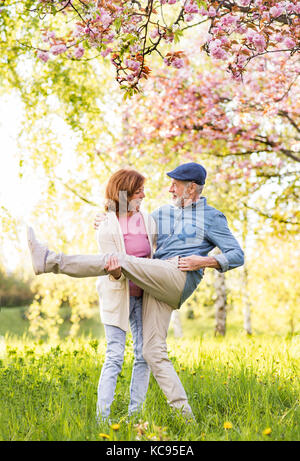 Beautiful senior couple in love on a walk outside, enjoying spring nature under blossoming trees. Man and woman having fun. Stock Photo