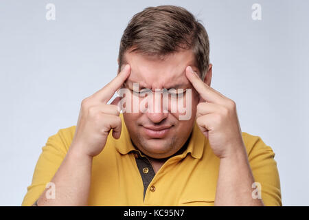 Stressed fat man in yellow t-shirt with fingers on temple suffering from headache. Stock Photo
