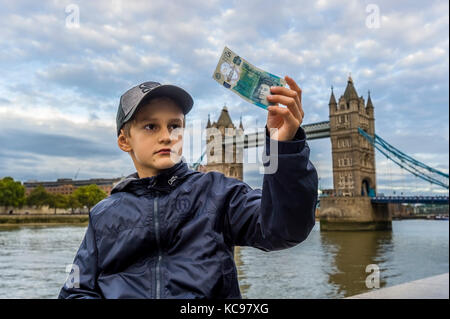 boy in baseball cap holding and looking at new british 5 pound banknote Stock Photo