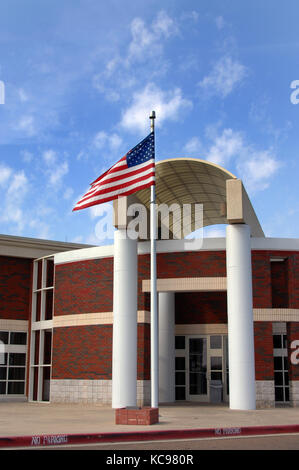 Post office building proudly flies the American Flag.  Building is two tone red and grey brick with white trim. Stock Photo