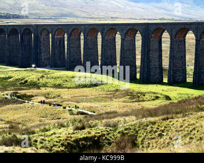 Walkers on a path under the Ribblehead Viaduct the largest viaduct on the Settle Carlisle railway line built 1870 to 1874 Yorkshire Dales England Stock Photo