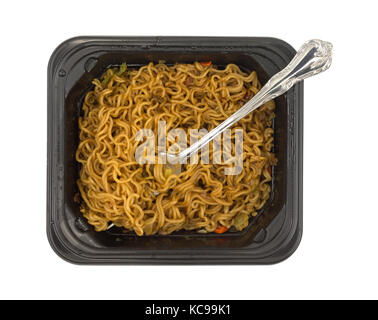Top view of a serving of beef flavored ramen noodles with a fork in a black microwavable tray isolated on a white background. Stock Photo