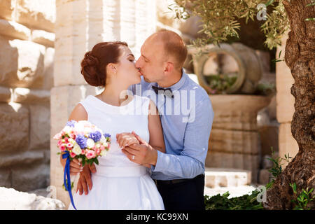 Bride and groom kissing outdoors. Wedding day of happy bridal couple, newlywed woman and man embracing with love in the park. Stock Photo