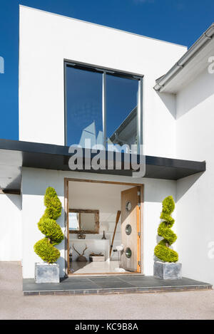 Stylish architectural entrance to contemporary seaside house with double doors open inwards exposing the hallway. Model Yacht in upper window. Stock Photo