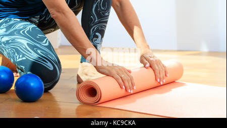 Fitness at home concept. Woman rolling an exercise mat on wooden floor Stock Photo