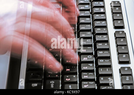 Motion blurred hands typing on computer keyboard Stock Photo