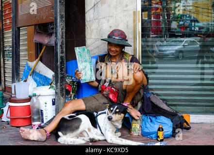 A homeless elderly Thai man sits with his dog outside a shop in Chinatown, Bangkok, Thailand Stock Photo