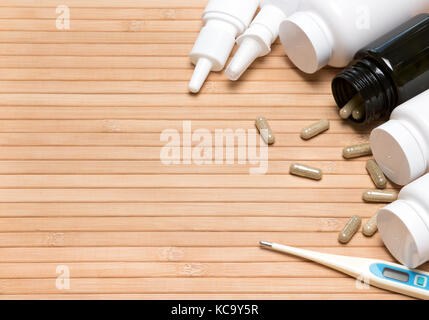 Treatment of cold and flu background. Scattered capsules, white plastic jars of medicines, nasal sprays, electronic thermometer. Copy space Stock Photo
