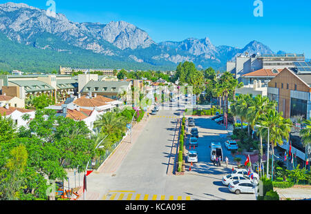 KEMER, TURKEY - MAY 12, 2017: One of the central streets of resort with lush green trees among the cozy family hotels and great mountain range on back Stock Photo