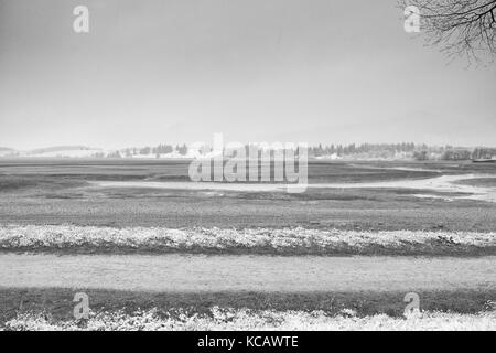 Straight  muddy tractor way. April weather. Wet spring snow in already fresh green meadows bellow mountains. Stock Photo