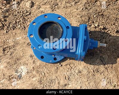 Detail of fittings, 150mm gate valves for drink water system. Repairing of piping in excavation pit. New blue painted gate valve on dry clay Stock Photo