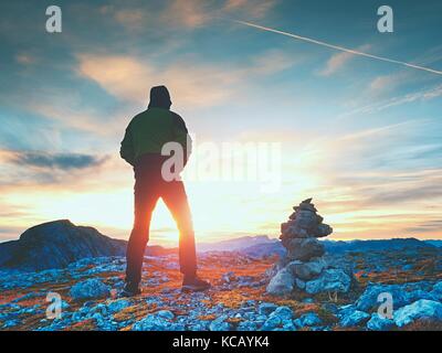 Stones pyramid on Alpine gravel mountain summit. Daybreak horizon above blue mist in valley. Mountains increased from horizoon Stock Photo