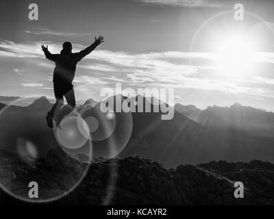 Lens flare effect. Bow light circles. Crazy hiker jumping at peak of mountain. Tourist jump on rock above  foggy valley. Mountains increased from humi Stock Photo