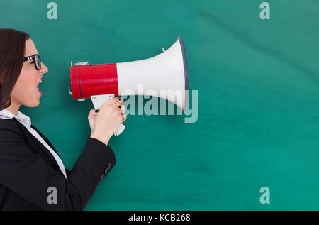 Young Businesswoman Shouting Through Megaphone Against Blackboard Stock Photo