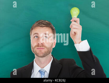 Portrait Of A Young Businessman Using Ecological Bulb Against Blackboard In A Classroom Stock Photo