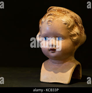 Close-up studio shot of vintage composition girl doll's head, shingled hair, and blue eyes. Sad expression. with copy space in black Stock Photo