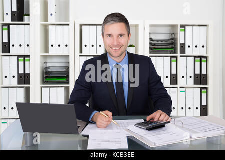 Successful Accountant  Calculating Tax Invoice At Office Desk Using Calculator And Laptop Stock Photo