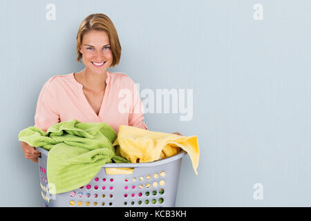 Portrait Of A Happy Woman Carrying Laundry Basket Against Colored Background Stock Photo