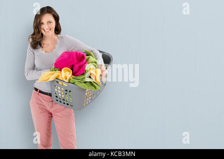 Portrait Of A Happy Woman Carrying Laundry Basket On Colored Background Stock Photo