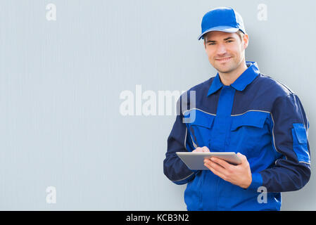 Portrait Of A Young Delivery Man Holding Clipboard On Colored Background Stock Photo