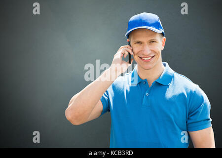 Happy Male  Delivery Man Using Cellphone On Gray Background Stock Photo