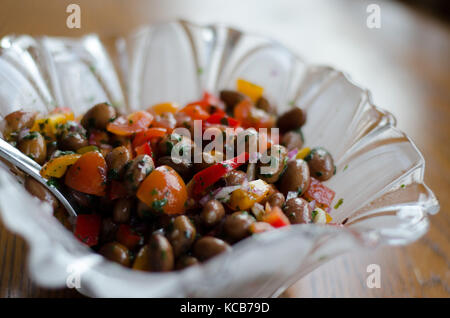 A bowl of glass with a colorful bean salad on a wooden table. Stock Photo