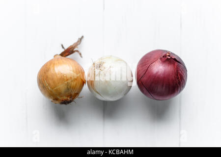 Three bulbs on a white wooden background. White onions, onions and red onions. Top view Stock Photo