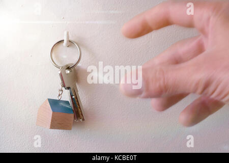Hands that are going to take keys from a house hung on a hook in the wall Stock Photo