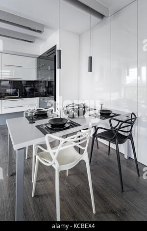 Home interior with white dining table, modern chairs and open kitchen Stock Photo