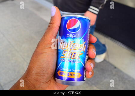 Shot of young black/brown woman's hand holding a can of Japanese Pepsi Refresh Shot Strong Cola on the streets of Japan with teenage boy in background Stock Photo