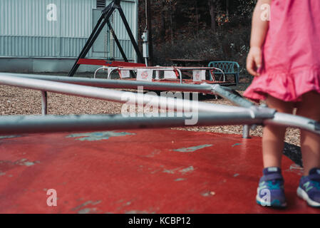 A toddler stands on a merry go round on a low income playground Stock Photo