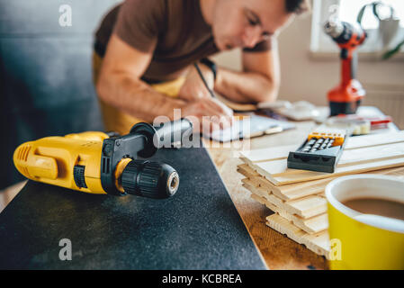 Yellow power drill and man making draft plan using pencil on the table with tools in the background Stock Photo