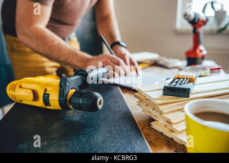 Yellow power drill and man making draft plan using pencil on the table with tools in the background Stock Photo