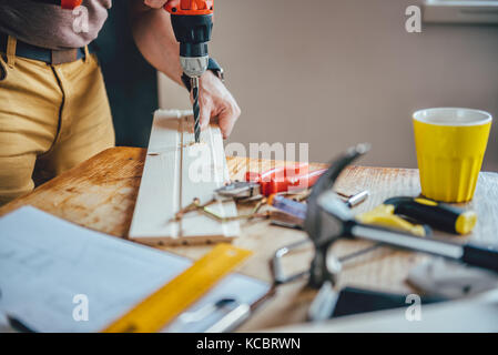 Man drilling wood with cordless drill on the table at home Stock Photo