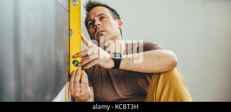 Man wearing brown shirt using leveling tool at home Stock Photo