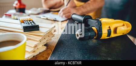 Yellow power drill and man making draft plan using pencil on the table with tools in the background Stock Photo