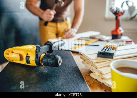 Yellow power drill and man using hammer on the table with tools in the background Stock Photo