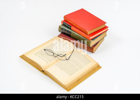 Open book isolated on white table with a stack of books and reading glasses. Stock Photo