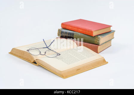 Open book isolated on white table with a stack of books and reading glasses. Stock Photo