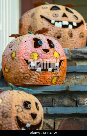 Vertical photo of decorated orange halloween pumpkins on the steps of a porch with the middle one in focus Stock Photo